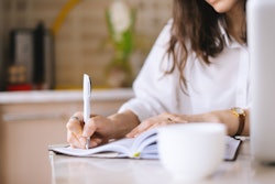 Close up of a woman writer hand writing in a notebook at home in the kitchen