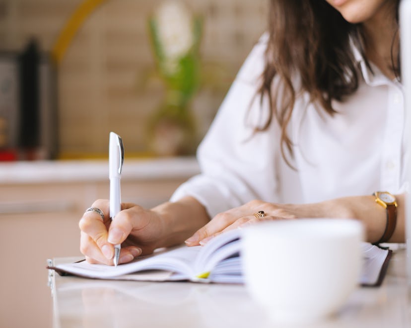 Close up of a woman writer hand writing in a notebook at home in the kitchen