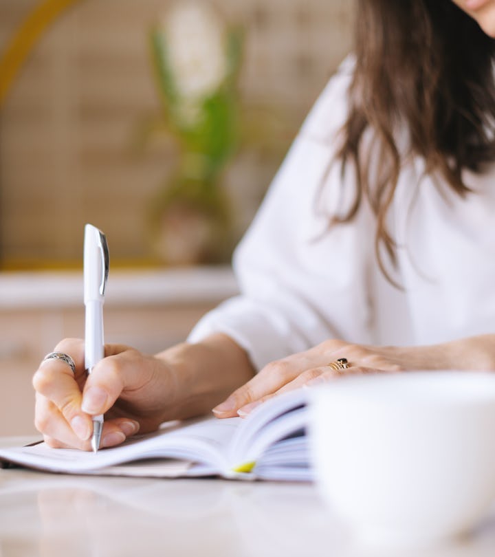 Close up of a woman writer hand writing in a notebook at home in the kitchen