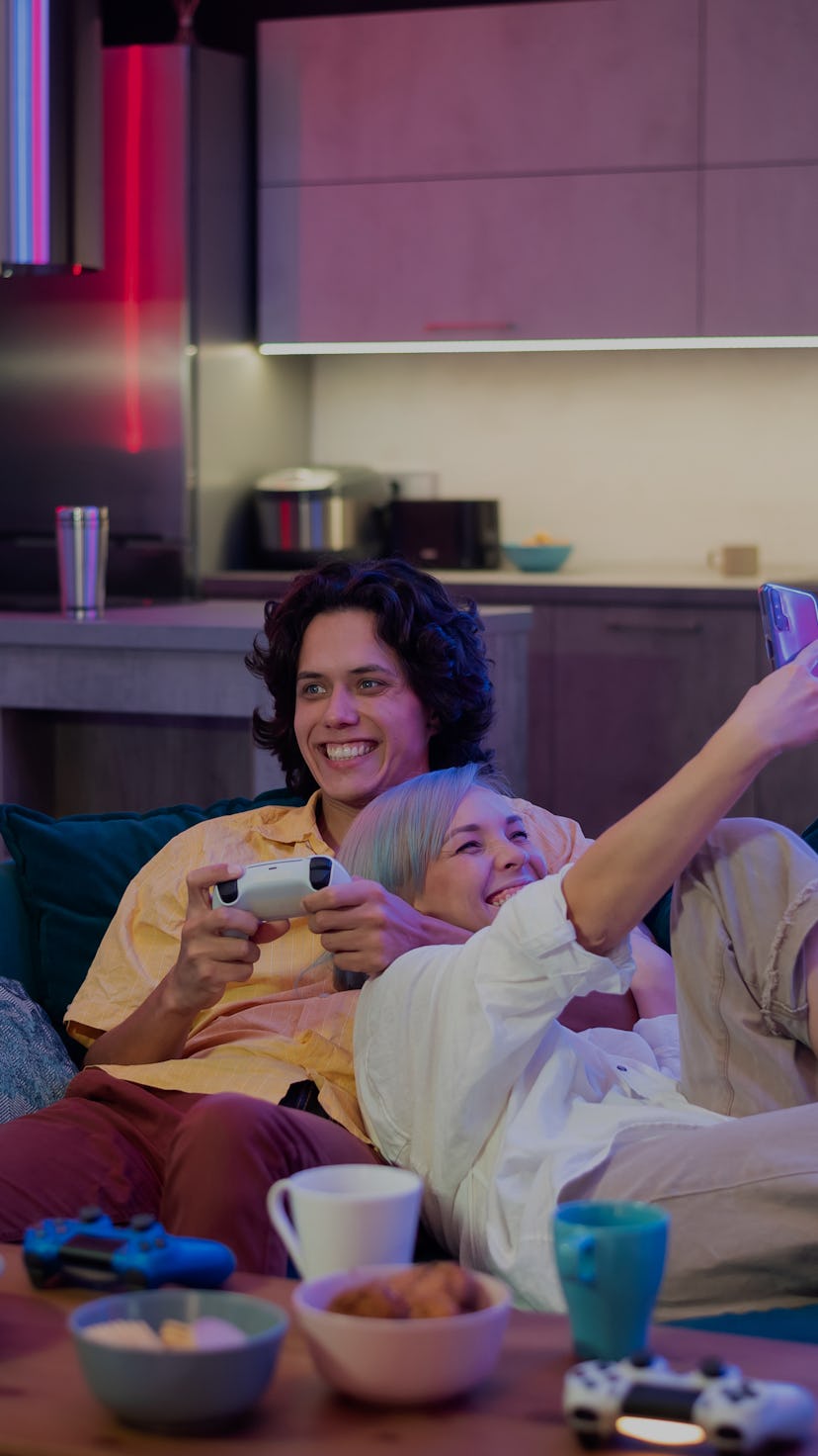 Guy playing video game while girl using smartphone for social media. Spending time together at home.