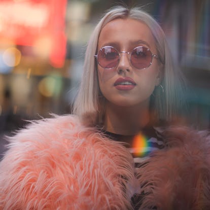 Young woman wearing a pink fur coat standing in a city street, knowing her zodiac sign will have the...