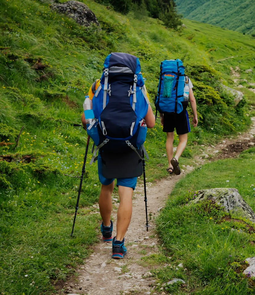 Hiking trail in Svaneti region, Georgia. Two hikers men walk on trek in mountain. Tourists with back...