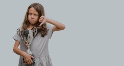 Brunette hispanic girl holding a trophy with angry face, negative sign showing dislike with thumbs d...