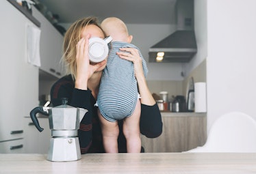 A mom downs a cup of coffee made from a moka pot while holding her infant