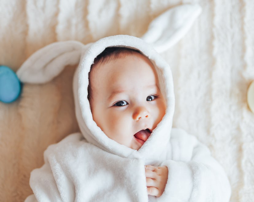 Little child wearing bunny costume on Easter day. baby holding colour eggs lying on bed at home, hav...