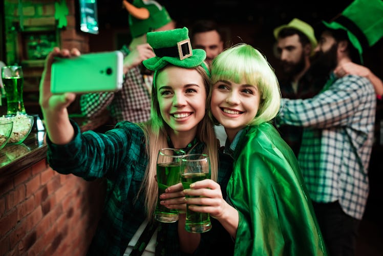 Two girls in a wig and hat take a selfie, which will need St. Patrick's Day 2022 captions for Instag...