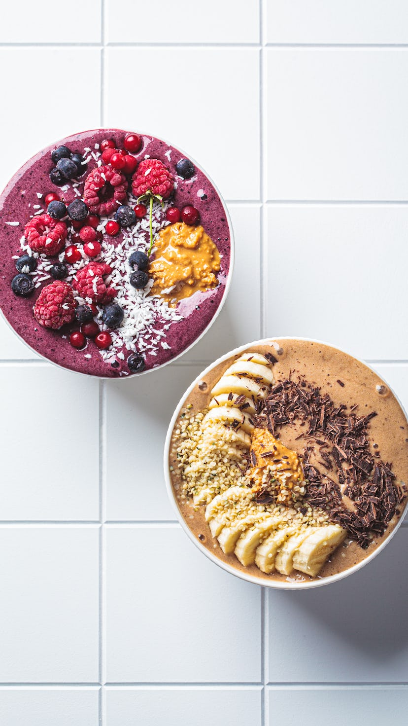Chocolate and berry smoothie bowls on a white tile background, copy space, top view. Raw vegan food ...