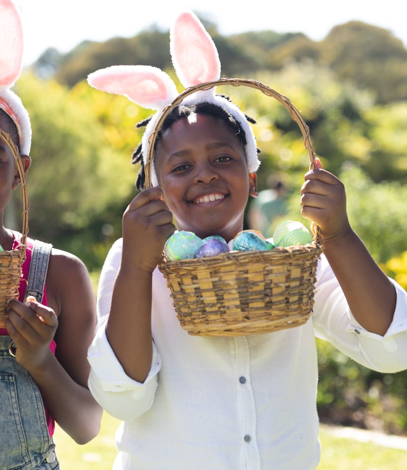 Happy african american brother and sister in bunny ears holding baskets of easter eggs. celebrating ...