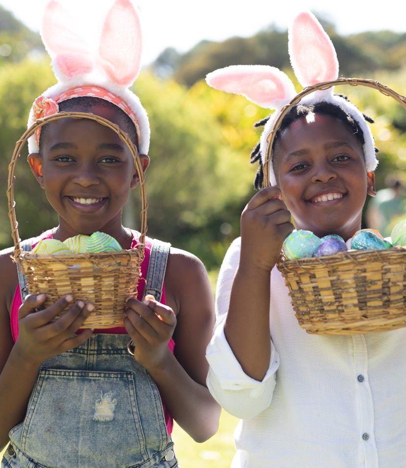 Happy african american brother and sister in bunny ears holding baskets of easter eggs. celebrating ...