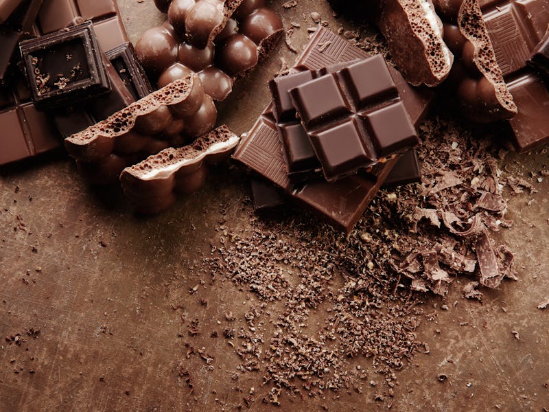 Composition of bars and pieces of different milk and dark chocolate, grated cocoa on a brown backgro...