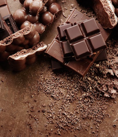 Composition of bars and pieces of different milk and dark chocolate, grated cocoa on a brown backgro...