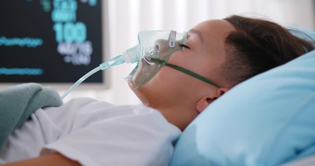 Close up sick young Black boy with face oxygen mask sleeping in bed at hospital.
