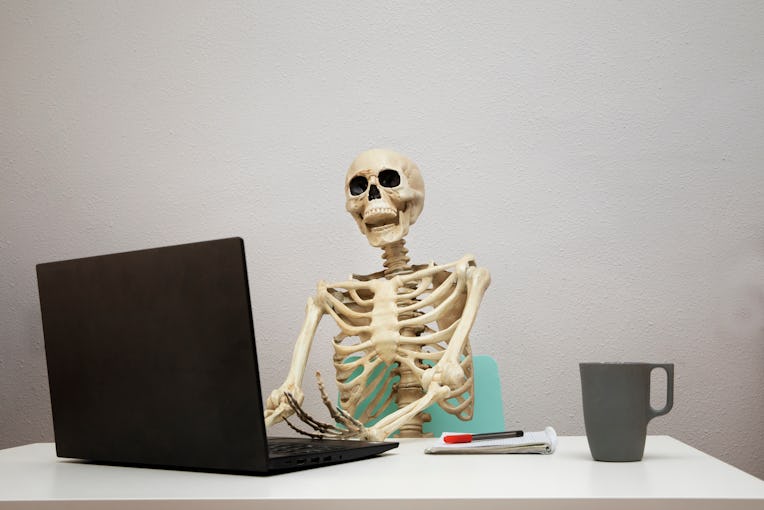 Bored at work: dead skeleton working at its home office.