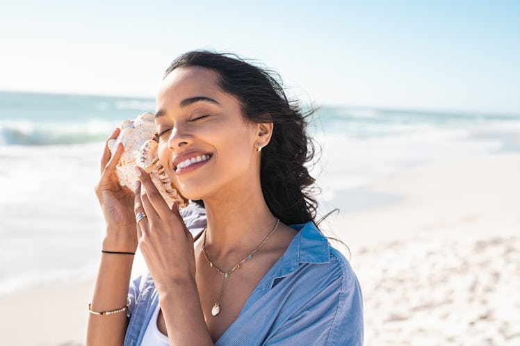 A woman listening to a conch, for which she needs seashells puns and quotes for Instagram captions.