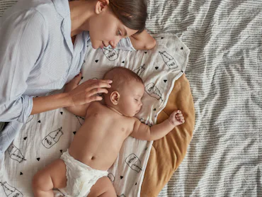 Portrait of lovely undressed angel like baby, peacefully sleeping near mother after breastfeeding in...