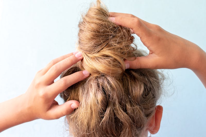 The girl straightens the disheveled bun on her head with her hands. Modern fast hairstyle. Blue back...