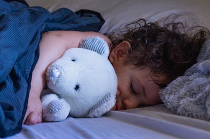Baby Hispanic girl with curly black hair and thick eyelashes takes a nap with her white teddy bear. 