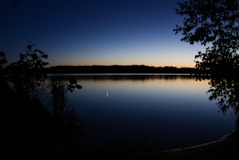 Two bright stars in the evening sky: their light reflects in calm lake surface and makes long tracks...