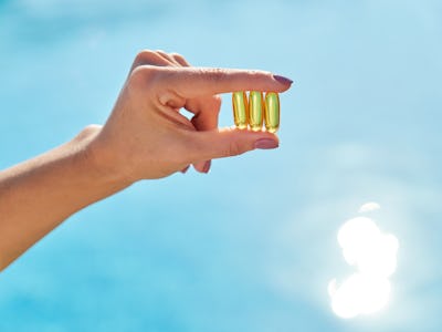 Sunny golden vitamin D oil capsules Omega-3 in woman hand, background sun blue water. Healthy lifest...