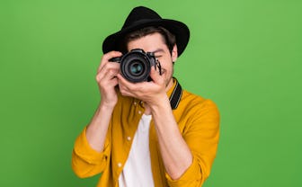 Photo of young handsome professional photographer take picture you camera isolated on green color ba...