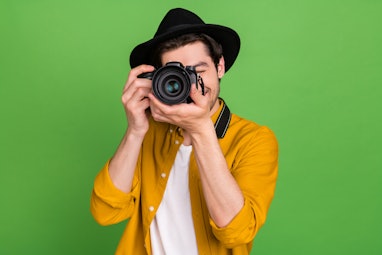 Photo of young handsome professional photographer take picture you camera isolated on green color ba...
