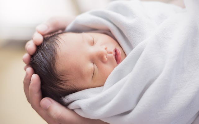 a parent's hands cup the head of a newborn baby