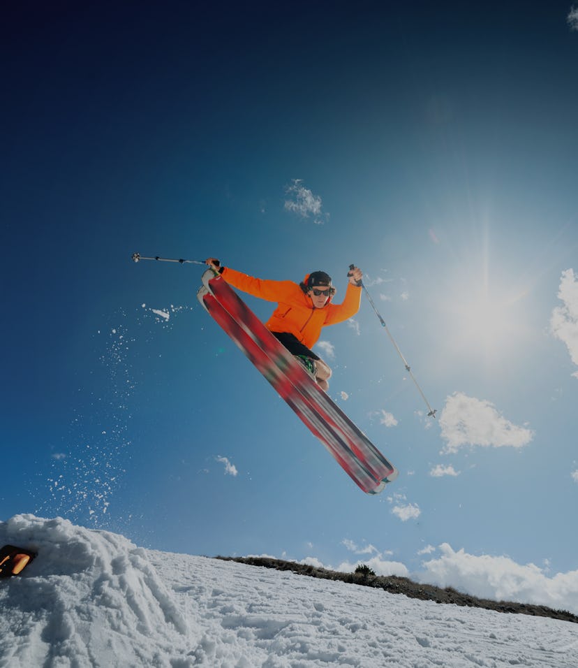 A young stylish man in sunglasses and a cap performs a trick in jumping with a kicker of snow agains...