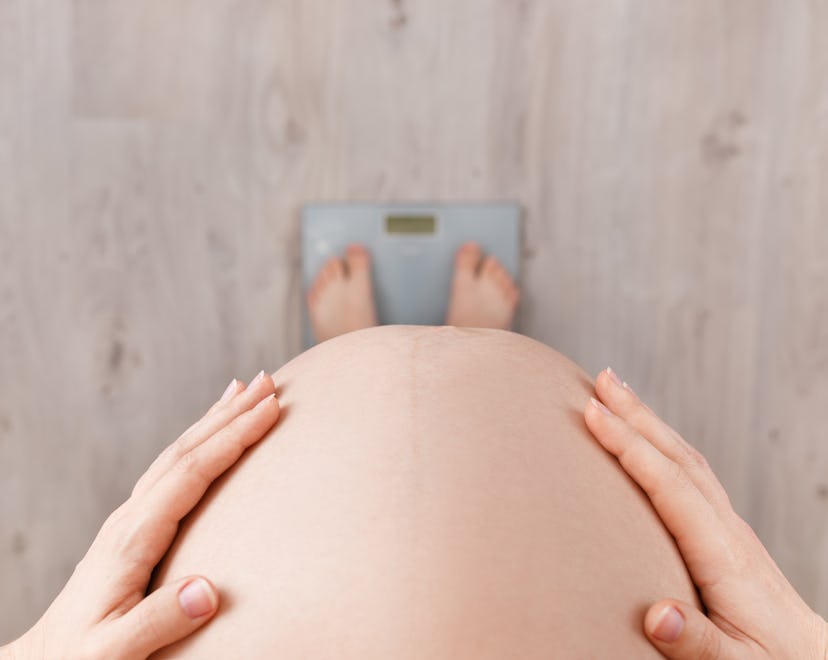 close up, overhead view of a pregnant woman's belly while she's standing on a scale, not gaining wei...