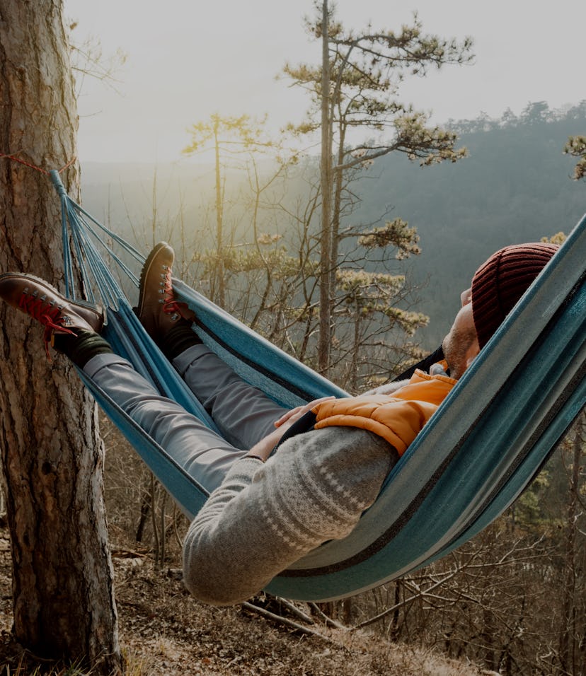Young happy man relaxing lying in hammock on top of mountain.