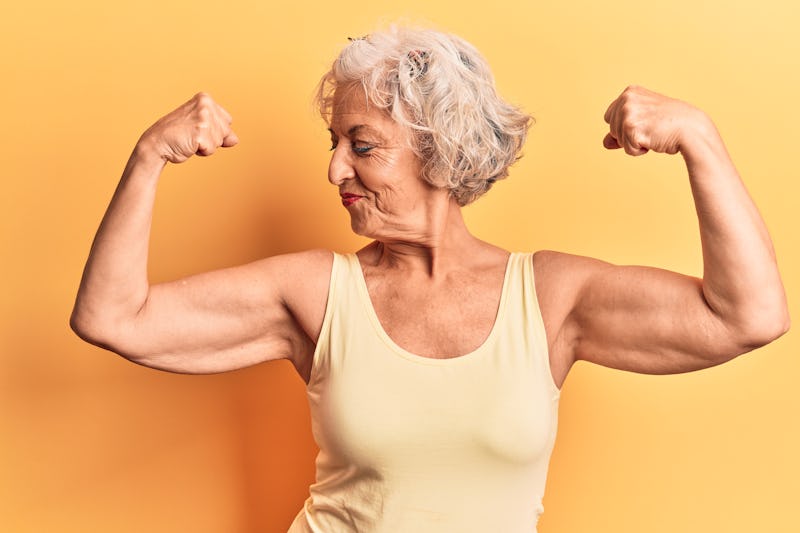 Senior grey-haired woman wearing casual clothes showing arms muscles smiling proud. fitness concept....