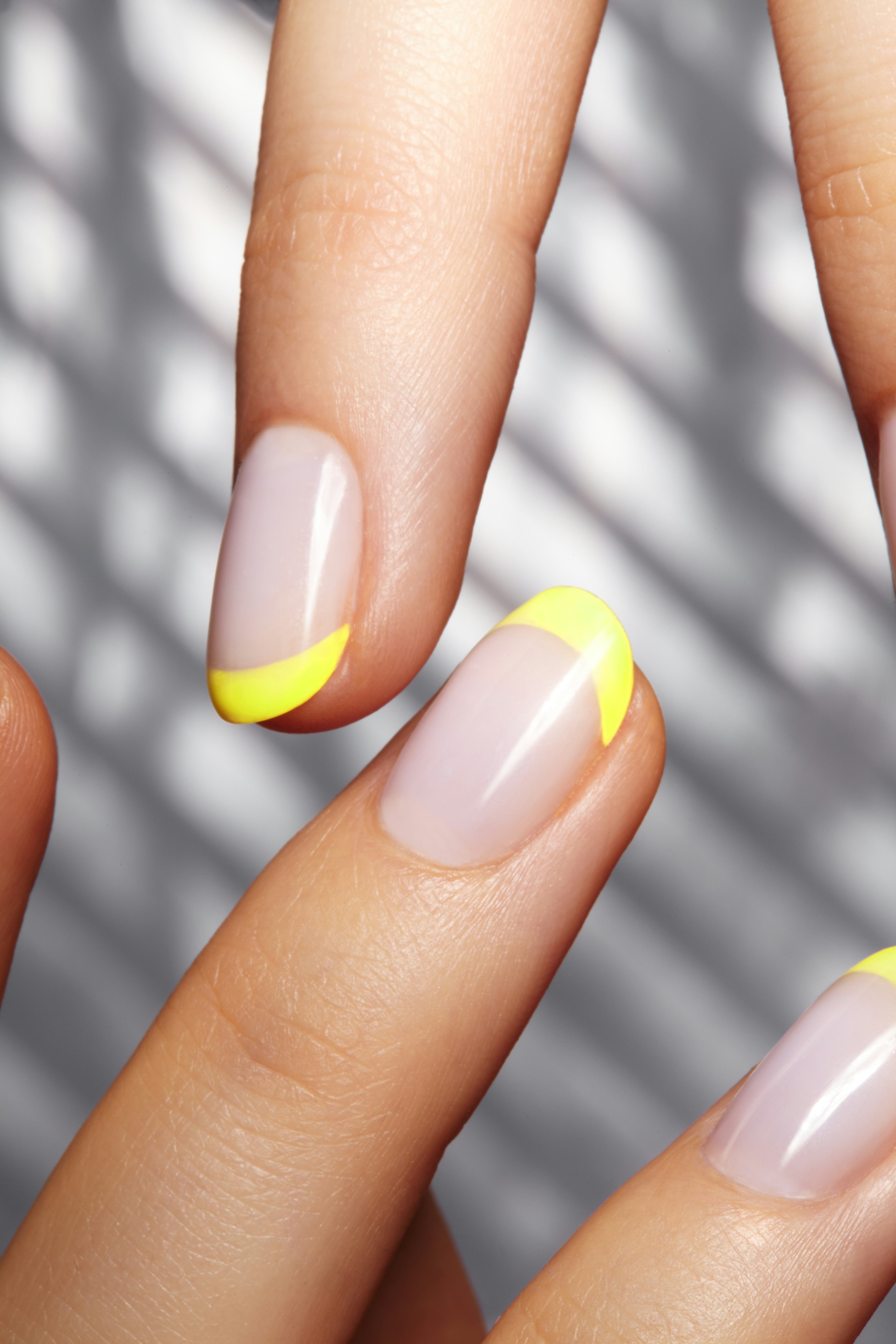 Hands with bright yellow french manicure on geometric background. Nails art design. Close-up of fema...