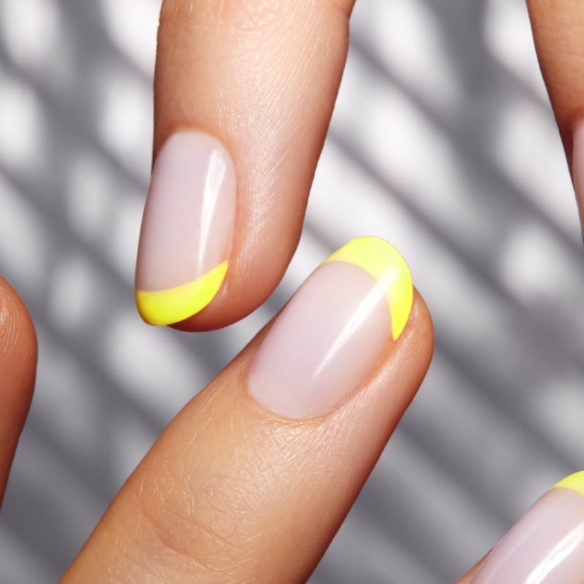 Hands with bright yellow french manicure on geometric background. Nails art design. Close-up of fema...