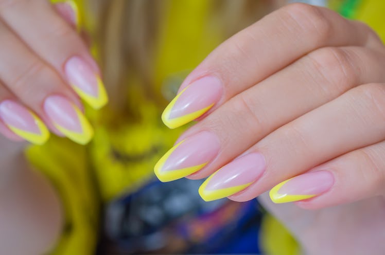 The hand of a young woman with spring 2022 nail trend French manicure of yellow color, nails in the ...