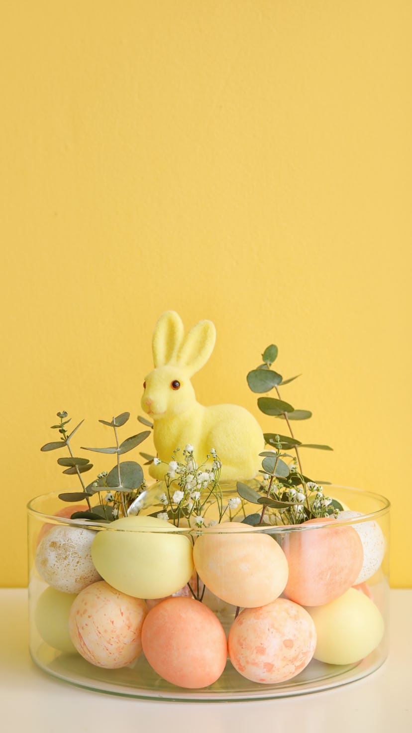 Bowl with Easter eggs, rabbit, and floral decor as Easter table setting.