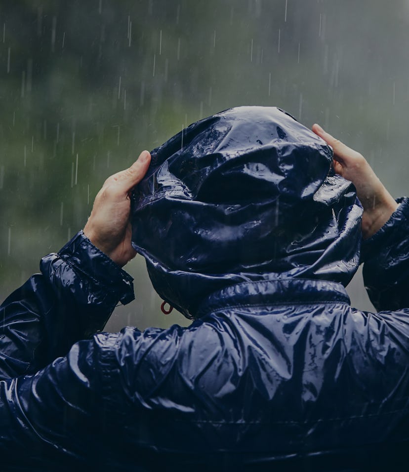 Trip in bad weather. Rear view of young man in drenched jacket in heavy rain.