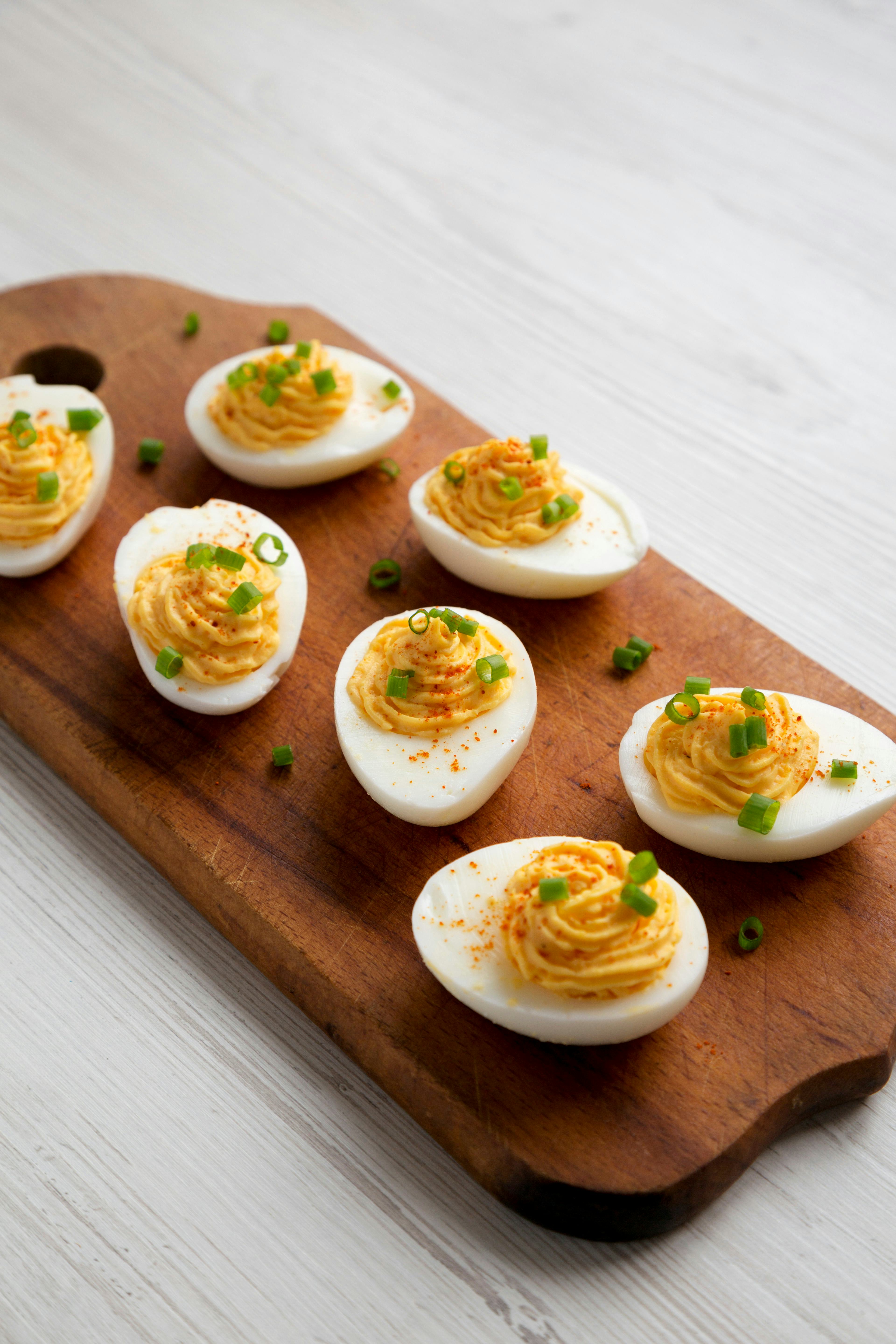 Homemade Deviled Eggs with Chives on a rustic wooden board on a white wooden background, side view. ...