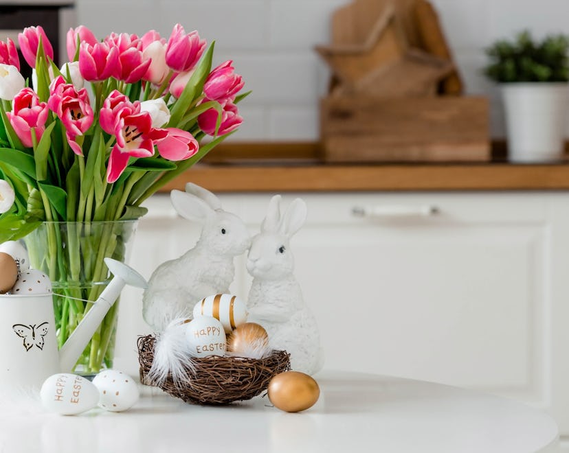 A bouquet of tulips, Easter bunnies, and eggs with a golden pattern on the table. 