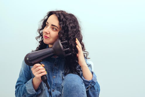 Woman using a modern hairdryer at home. Woman makes herself curly hairstyle. Beauty and haircare con...