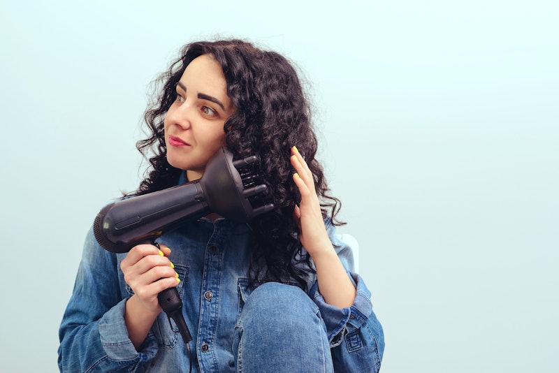 Woman using a modern hairdryer at home. Woman makes herself curly hairstyle. Beauty and haircare con...