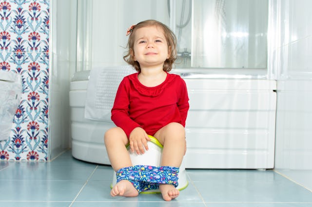 Beautiful little baby sit on potty in bathroom and cry. Cute adorable funny child girl using chamber...