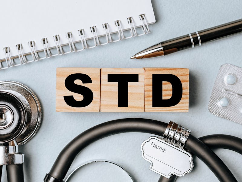Wooden block form the word STD with stethoscope, pills, notepad, pen on the doctor's desktop. Medica...