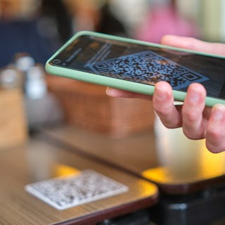 Closeup of guest hand ordering meal in restaurant while scanning qr code with mobile phone for onlin...