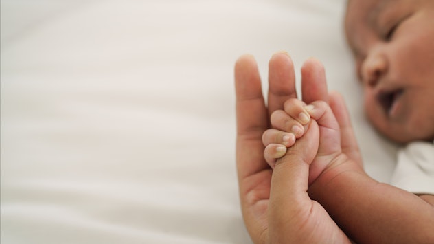 newborn baby hand holding mom finger on white bed in article of baby girl names that start with w