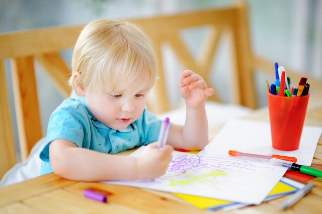 Cute little boy drawing and painting with colorful markers pens at kindergarten. Creative kid painti...