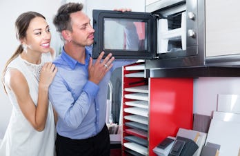 Smiling family couple looking for new modern mini oven in furniture showroom