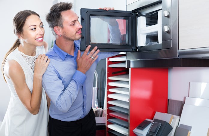 Smiling family couple looking for new modern mini oven in furniture showroom