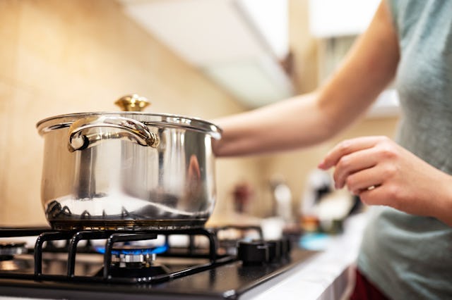 Beautiful young woman housewife prepairing dinner, hold in hands big steel saucepan, standing it on ...