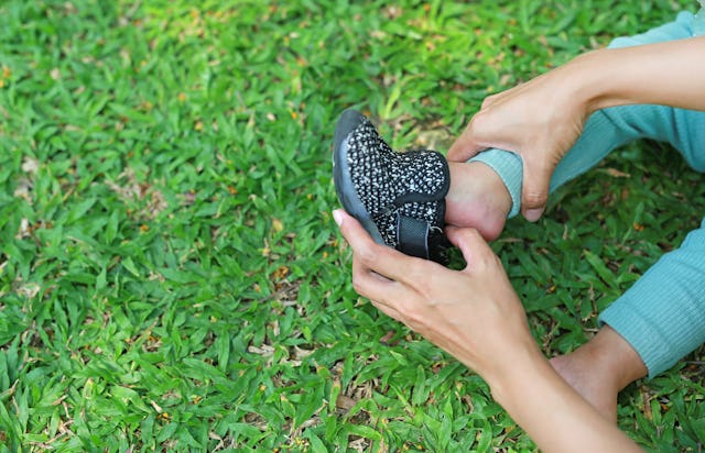 Hands of mother helping her baby to put shoes in the garden outdoor.