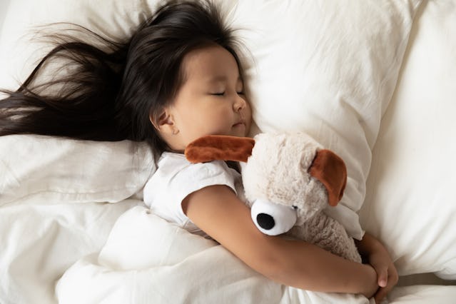 Close up top view lying in bed toddler asian girl hugs her favorite plush animal dog toy sleeping ca...