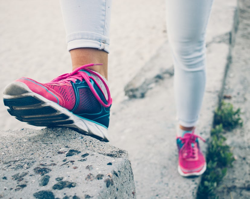 Female legs in sneakers and jeans standing on a concrete curb, toned image